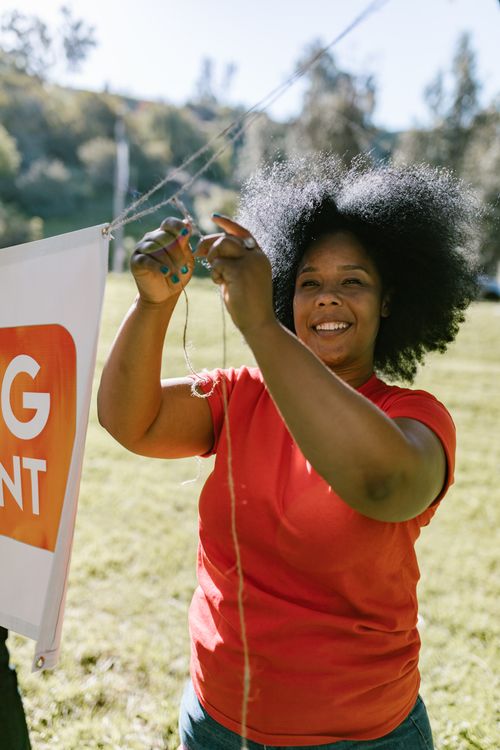 Free Woman with afro hair smiling during an outdoor team-building event, enjoying the sunny day. Stock Photo