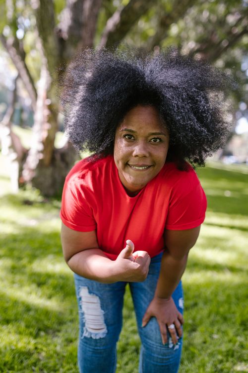 Free Smiling woman with afro hair enjoys a sunny day in the park, showing excitement and happiness. Stock Photo