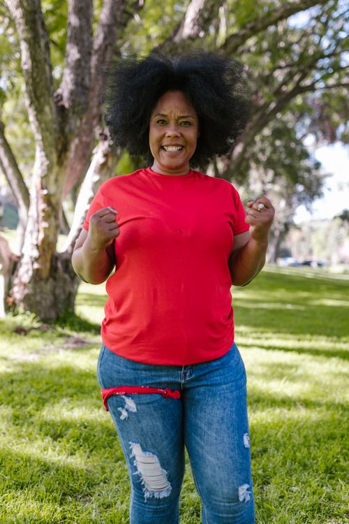 Free Smiling woman with afro hair celebrating in a sunny park, expressing happiness and leisure. Stock Photo