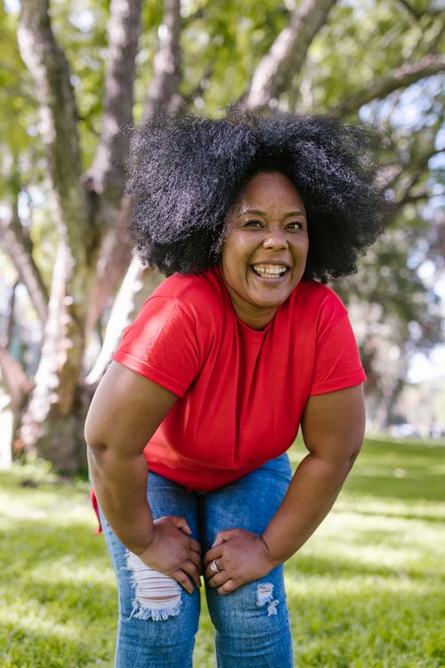Free Smiling woman with afro hair enjoying a sunny day in the park, embodying happiness and leisure. Stock Photo