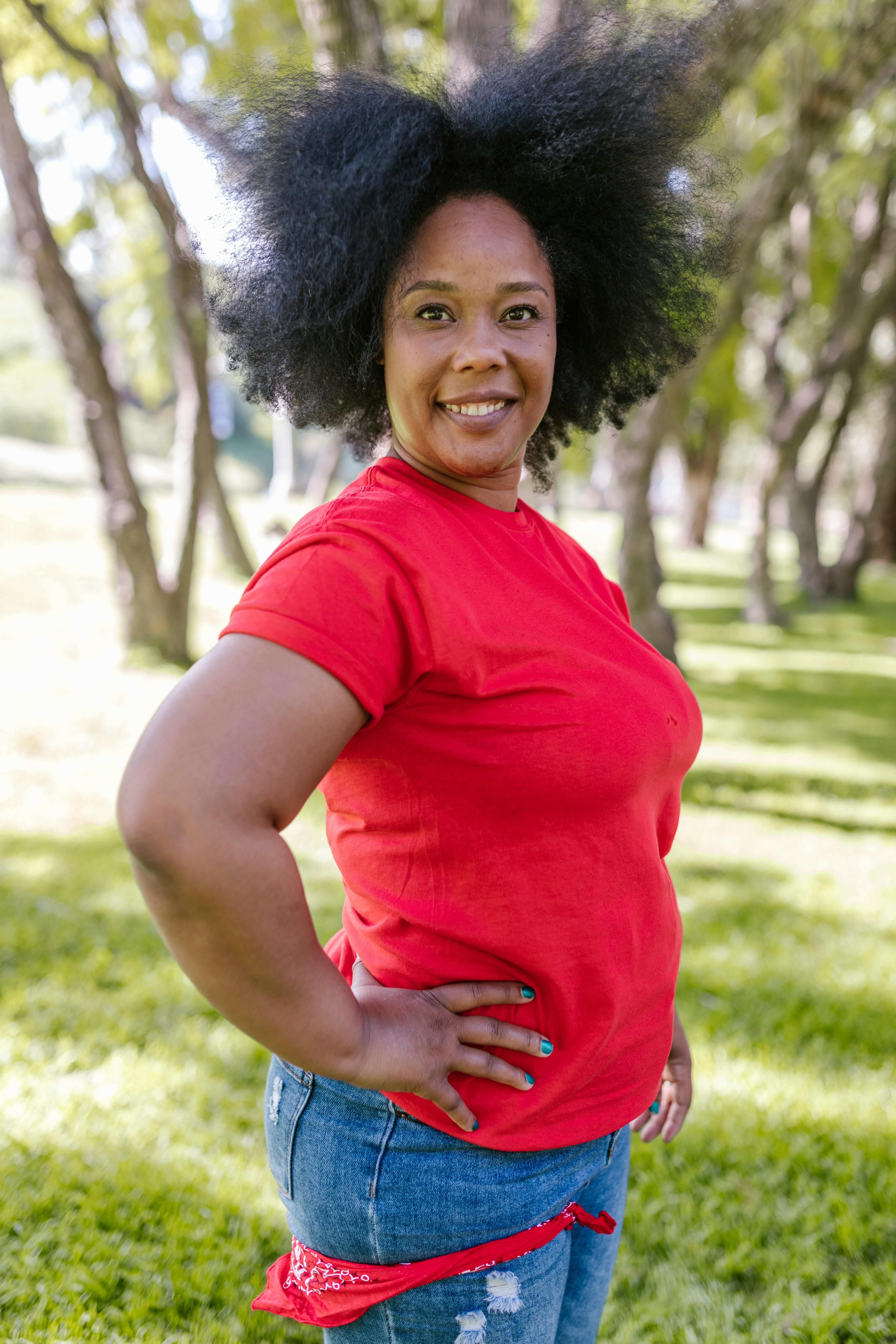A cheerful African American woman with afro hair smiling outdoors on a sunny day.
