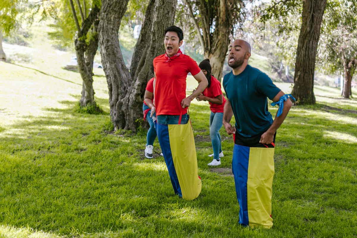 Adults competing in a sack race while teammates cheer