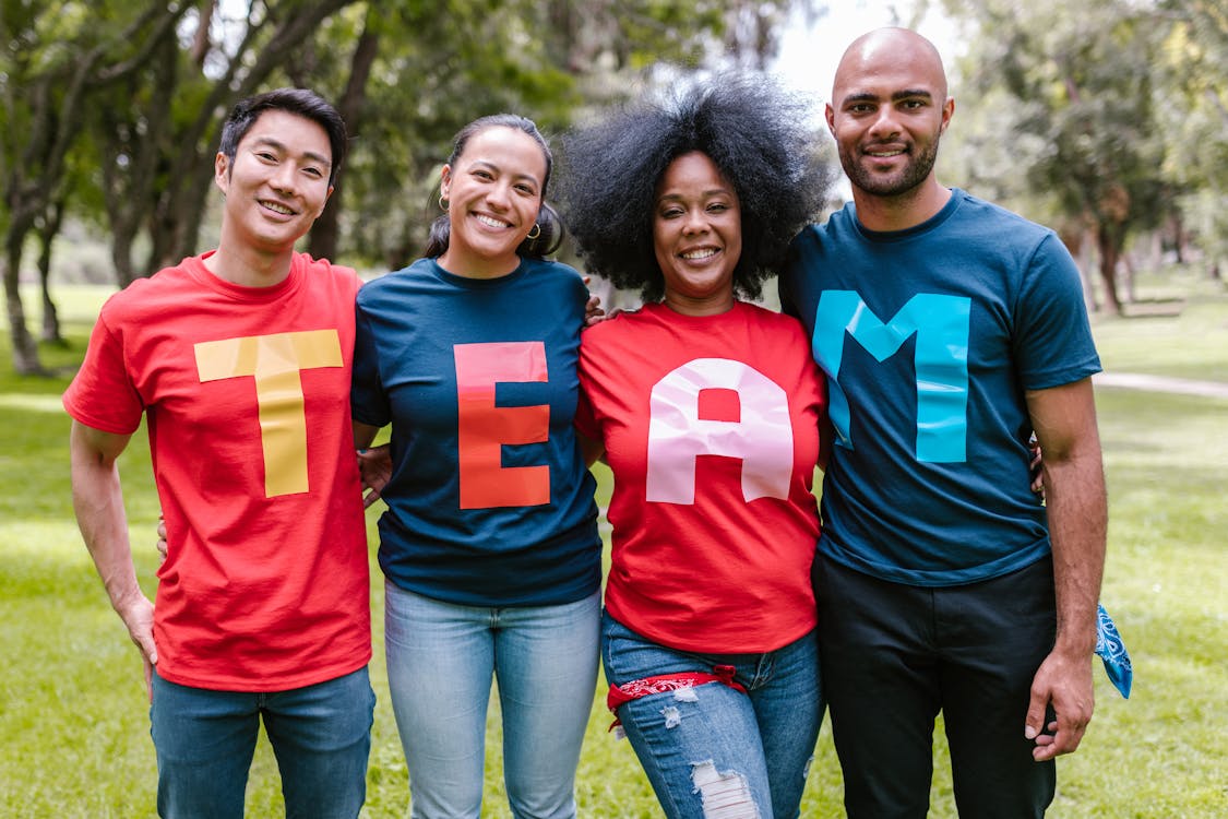 Four People Wearing Alphabet Shirts Spelling Out “Team” Representing the Team Effort in Real Estate
