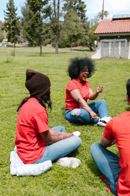 People in Red T-shirts Sitting on Green Grass
