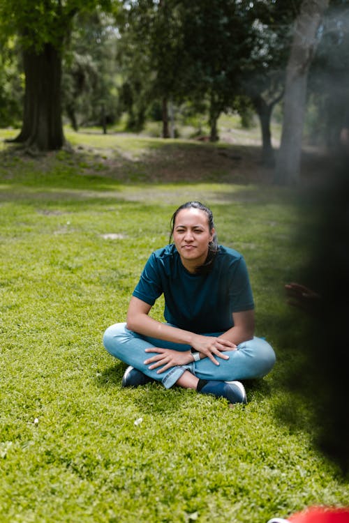 Woman in Blue Crew Neck T-shirt and Blue Denim Jeans Sitting on Green Grass 