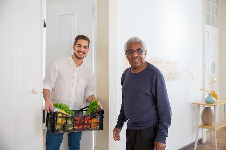 A Man Holding A Plastic Crate With Fruits And Vegetables