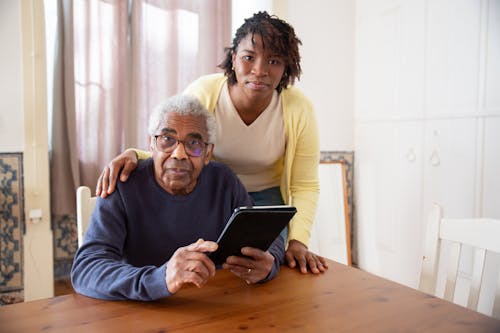 Free A Woman Standing Beside the Elderly Man Holding a Tablet Stock Photo