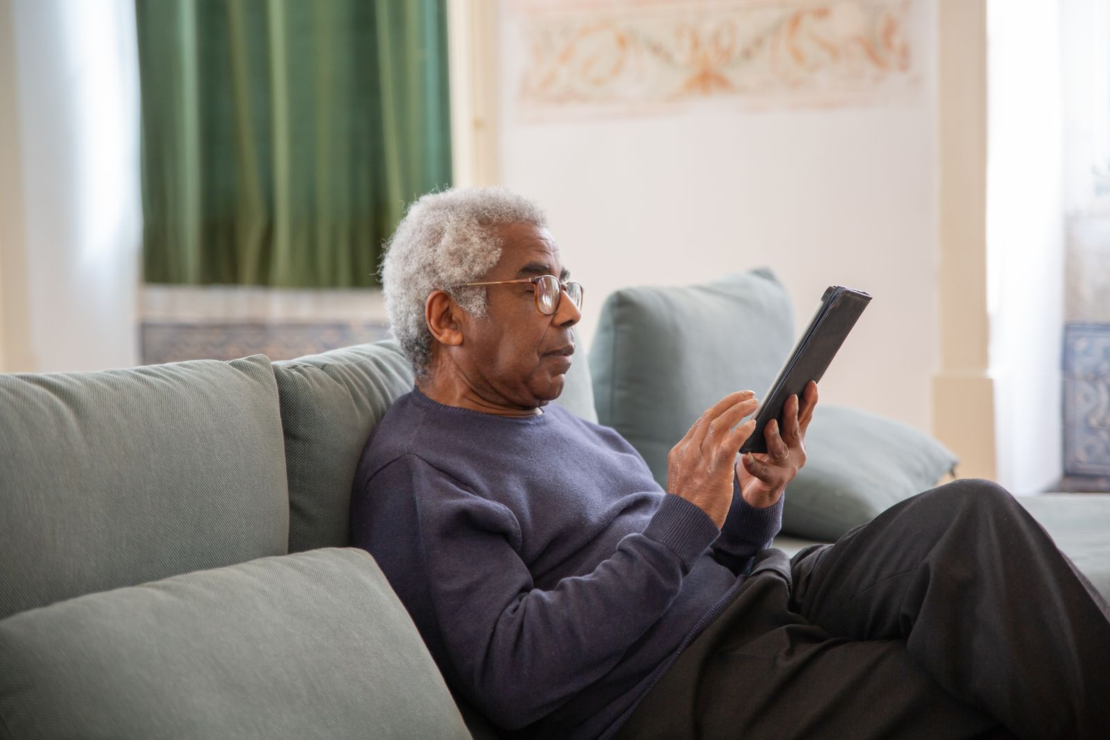 Homme senior lisant attentivement sur sa tablette chez lui
