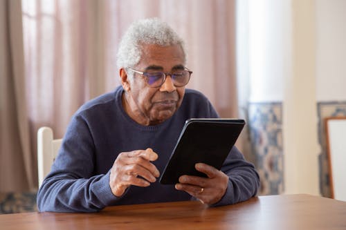 Free An Elderly Man in Black Sweater Using a Digital Tablet Stock Photo
