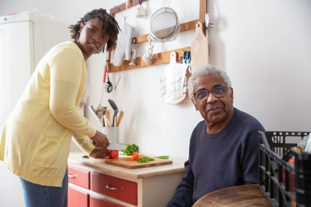 A care worker prepares a meal alongside an older gentleman in a kitchen