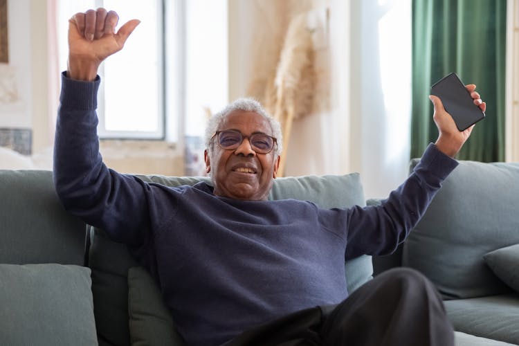 Elderly Man Sitting On Sofa While Holding A Cellphone