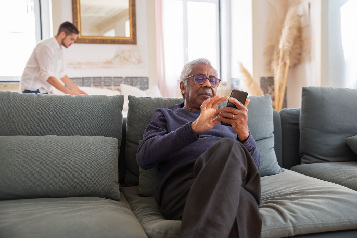 An adult child and older parent talk calmly on a sofa in a bright living room