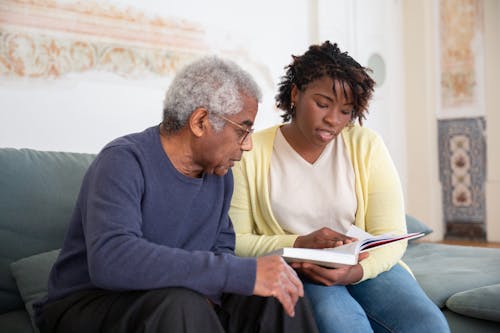 Free A Woman Reading a Book while Sitting Beside the Man in Blue Sweater Stock Photo