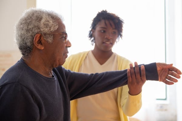 Caregiver helping elderly man with arm exercises at home