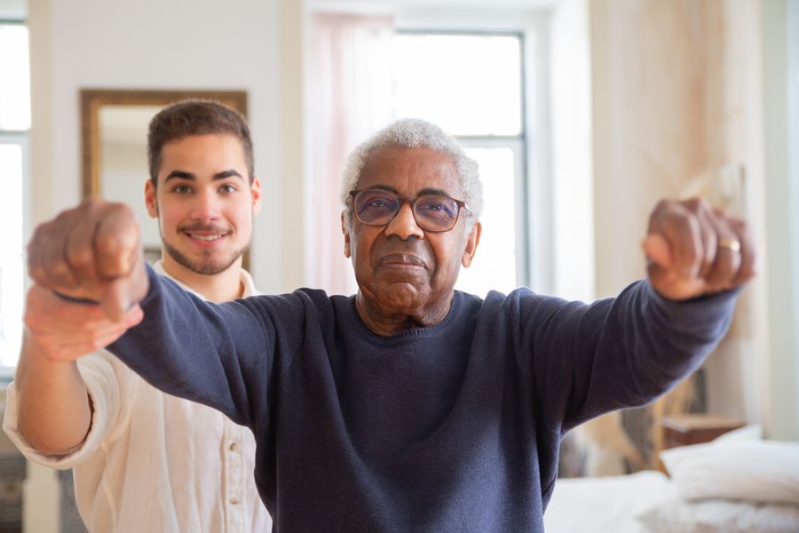 A resident being supported with a balance exercise by a caregiver