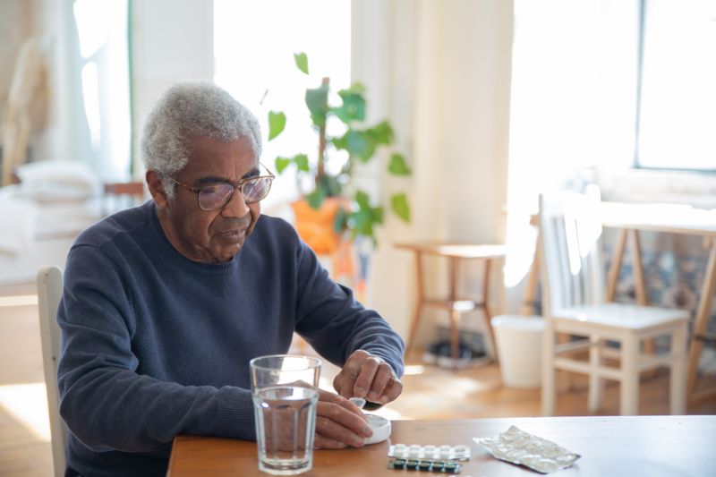An older Black man takes his medication at home. Controlling blood pressure and quitting smoking are the two biggest things that slow an aortic aneurysm.