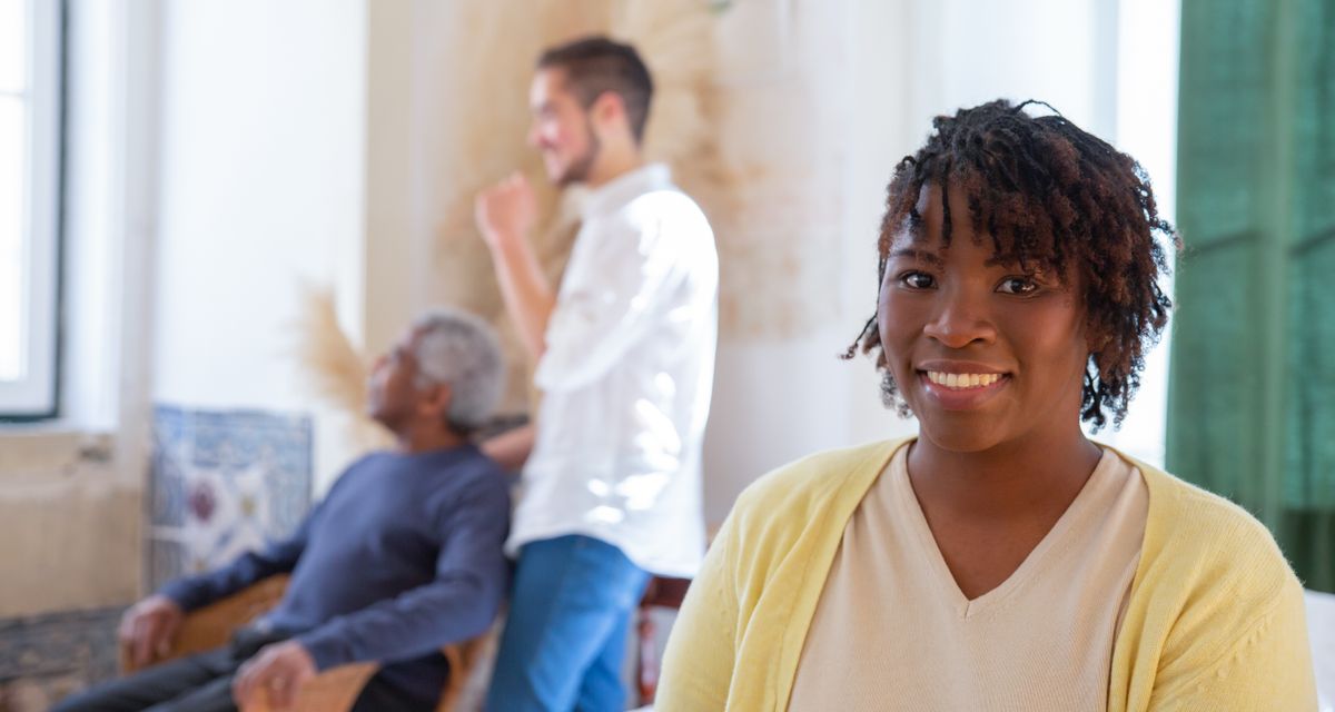 A smiling caregiver with an older man settling comfortably in a bright, welcoming room