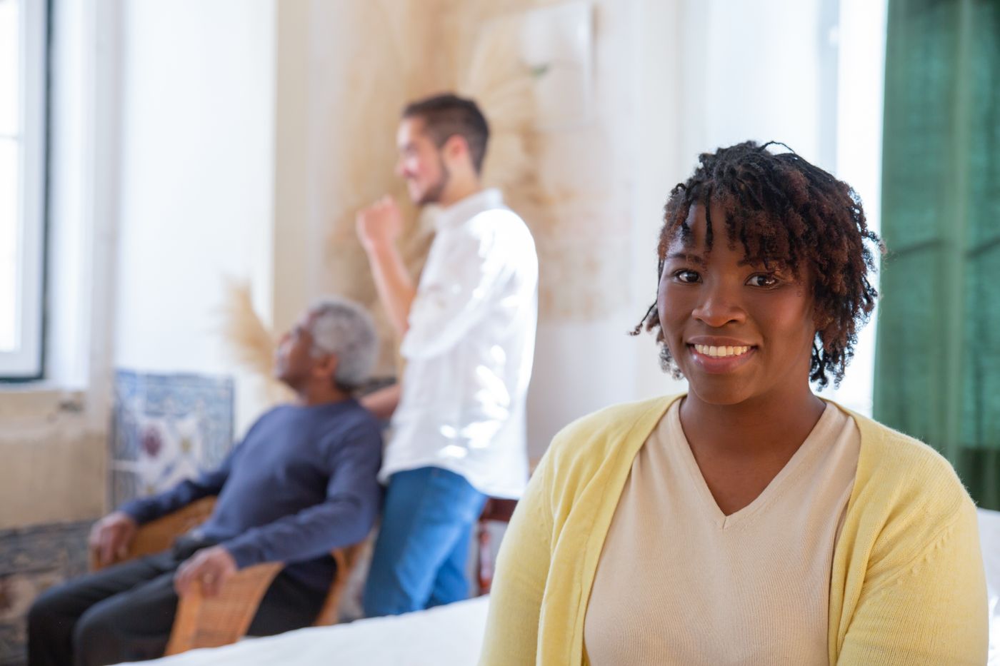 A family caregiver stands near an older adult and a local helper in a bright home