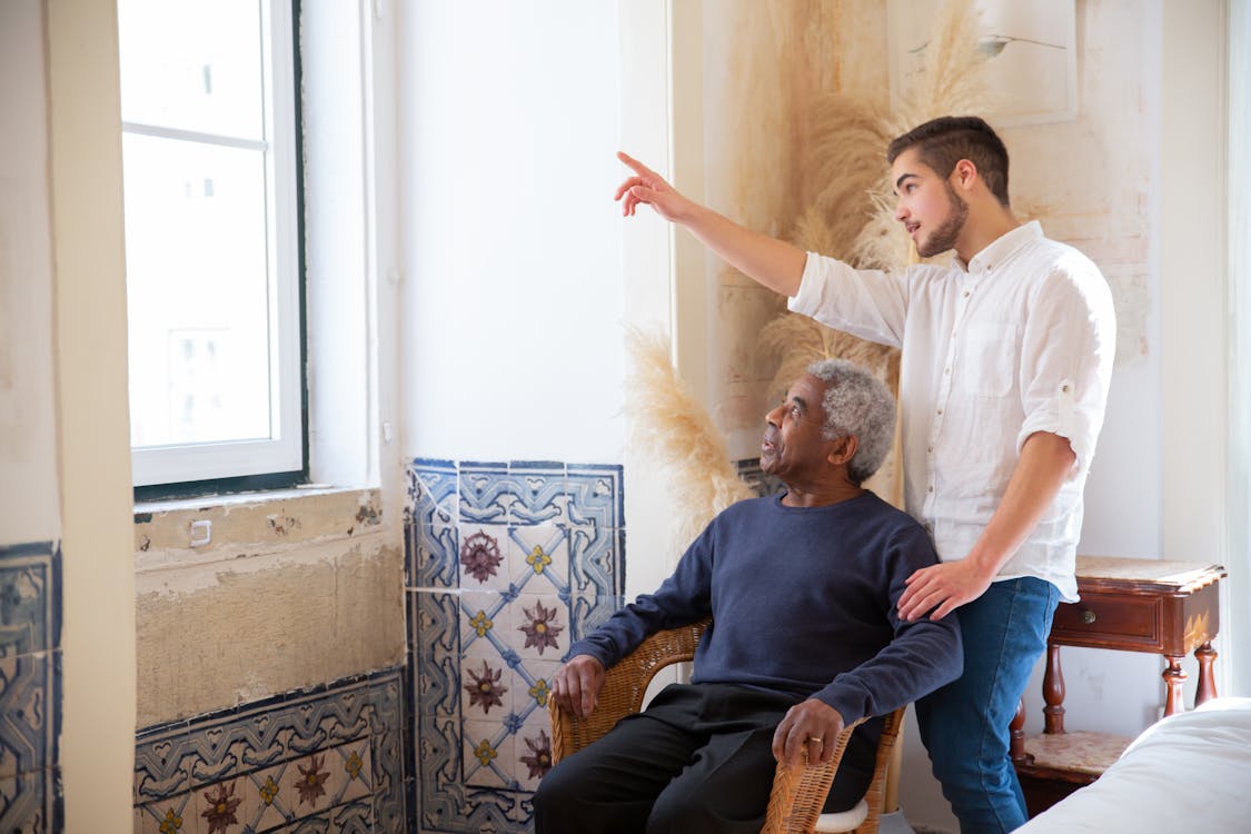 Free A Man in White Shirt and an Elderly Sitting on the Chair Looking at the Window Stock Photo