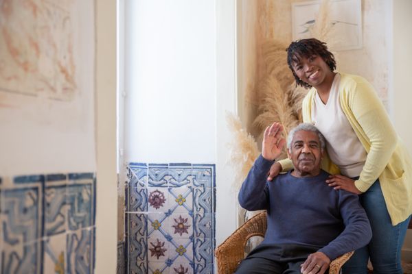 Caregiver and elderly man reading together on sofa at home
