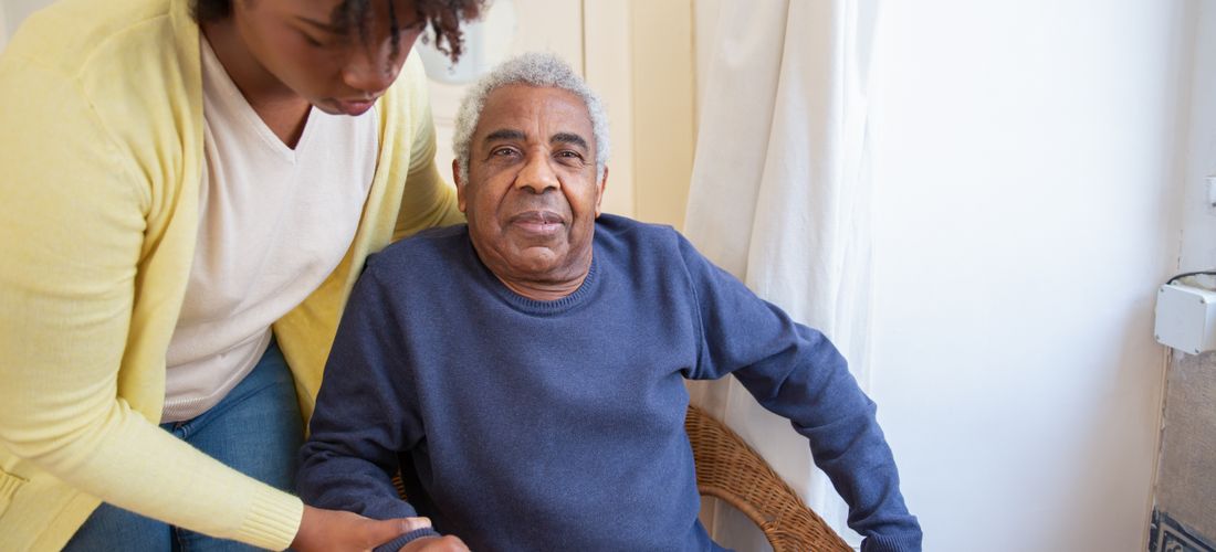 Caregiver helping an elderly woman walk through a sunny garden pathway