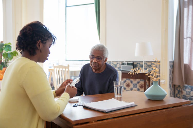 A Woman In Yellow Sweater Preparing Medicine For An Elderly Man