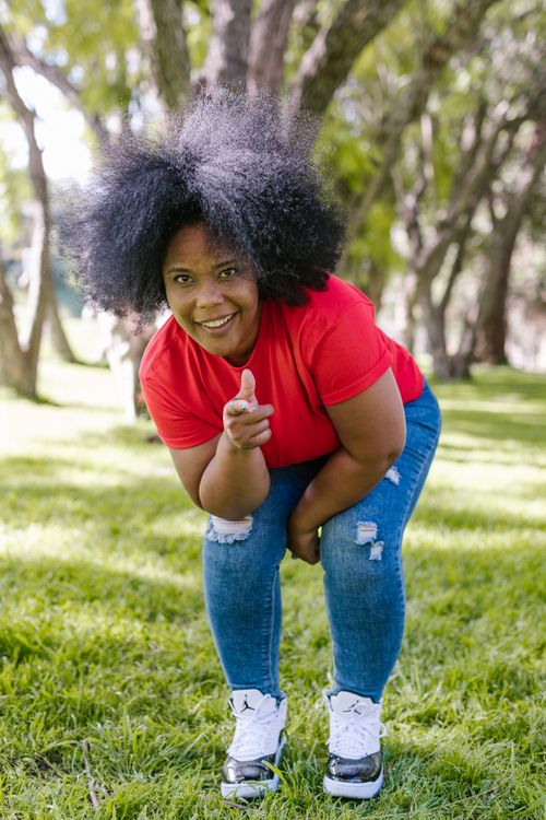 Free Woman with afro hair poses cheerfully in a sunny park wearing casual clothes. Stock Photo