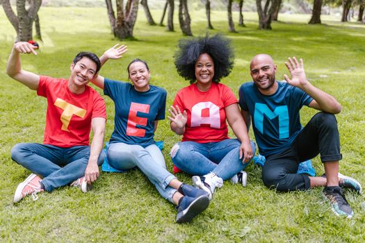 Multiracial team sitting on grass in park, wearing 'TEAM' shirts, showing unity.