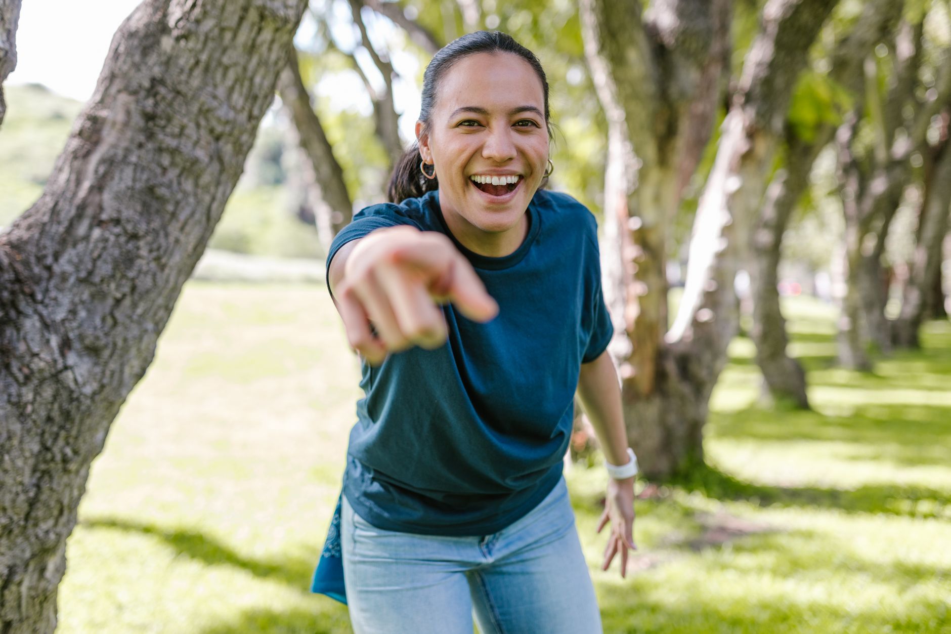 Smiling woman in park pointing happily on a sunny day.