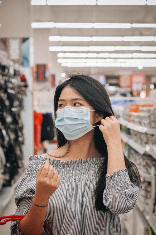 Free Young woman with black hair wearing a surgical mask shopping indoors in a store. Stock Photo