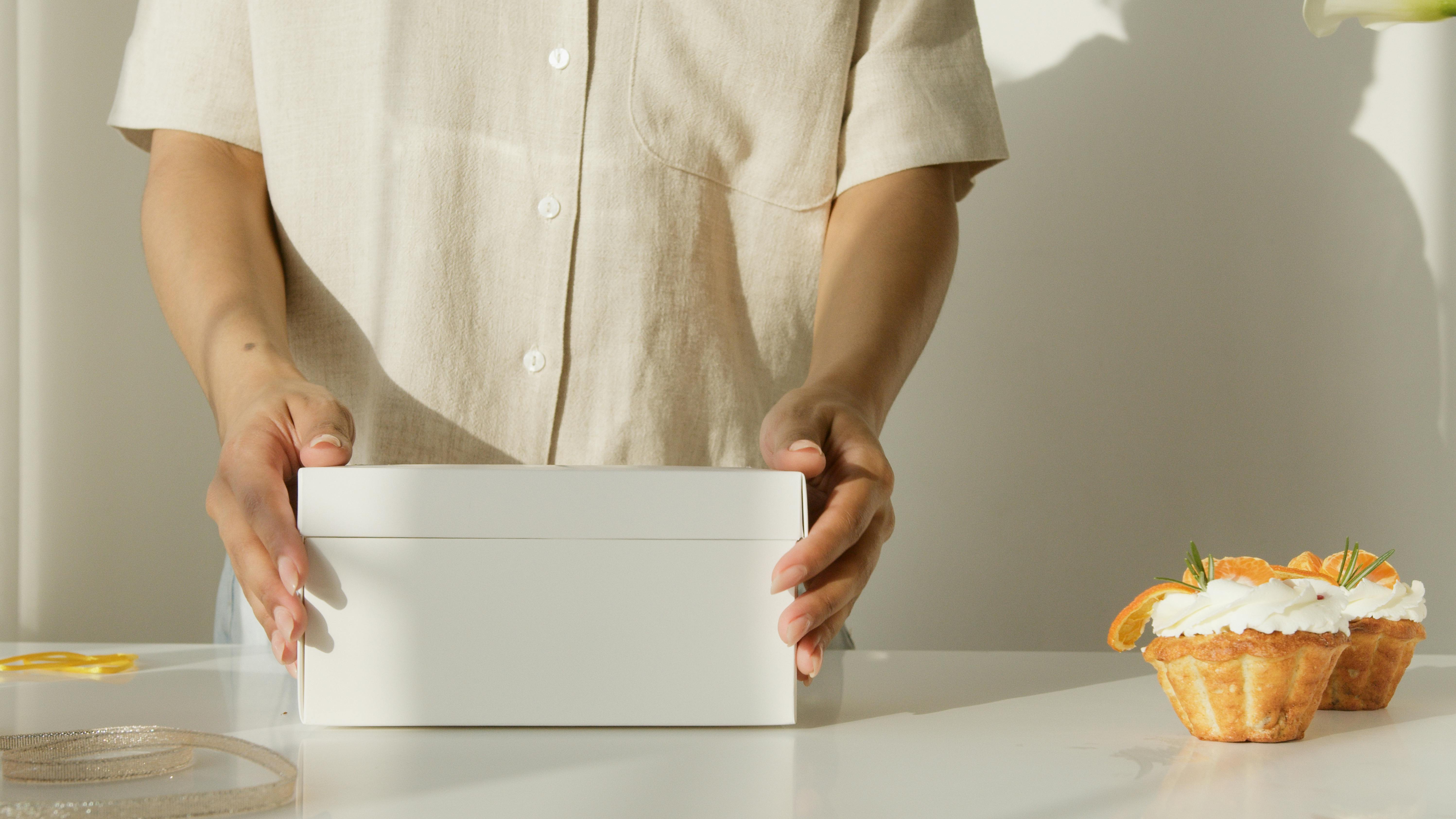 a person holding a white box near cupcakes