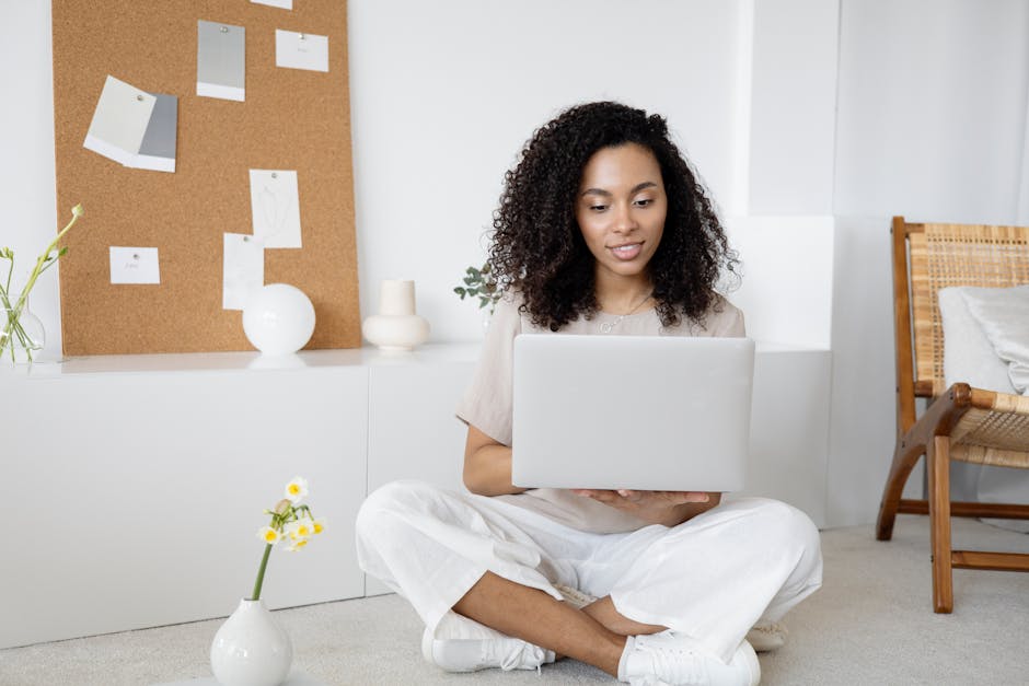 Woman in White Dress Shirt and White Pants Sitting on Floor Using Macbook