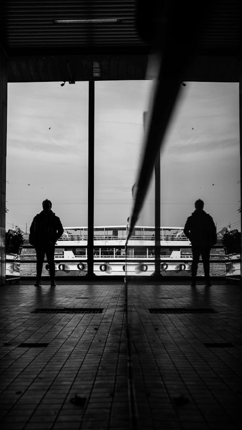 Monochrome Photo of Person Standing on Glass Wall 