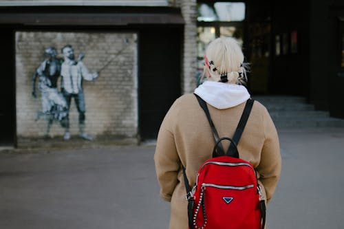 Blonde Woman with Red Backpack in Front of Graffitied Wall