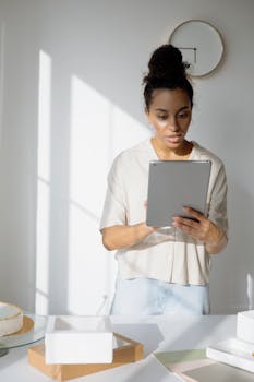 Young woman using tablet in a bright home office setting, managing online business.