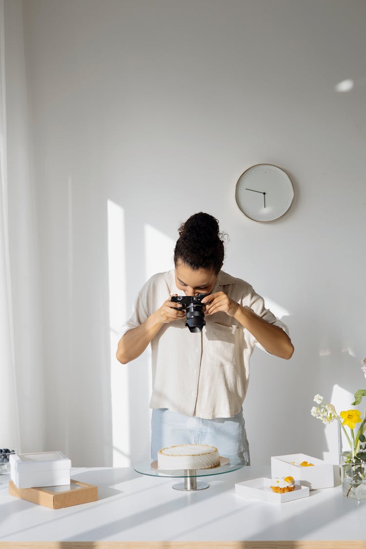 A Woman Taking A Picture Of A White Cake