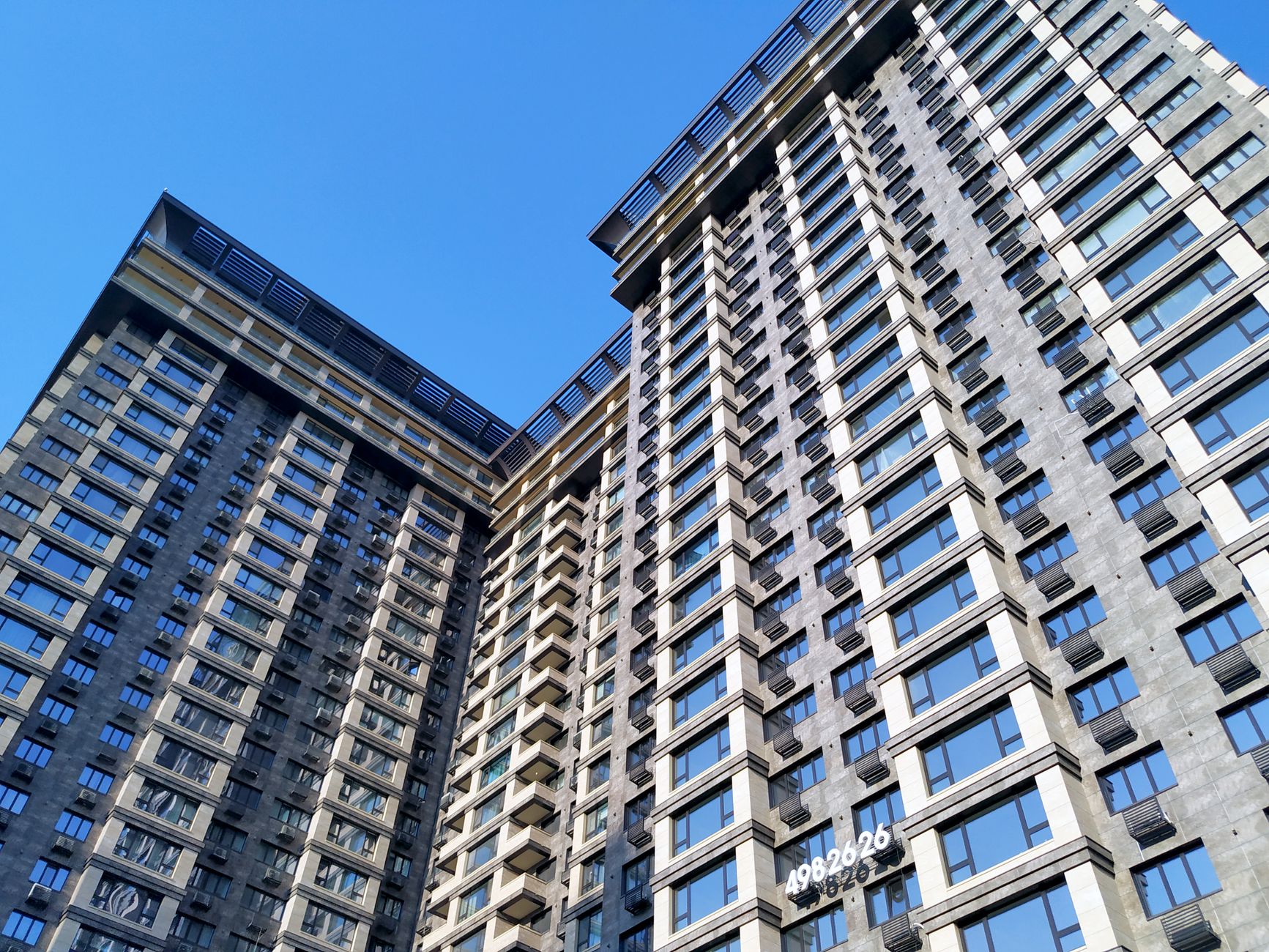 Low angle view of contemporary apartment buildings with glass windows against a clear blue sky.