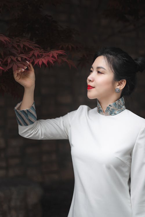 Woman in a White Long Sleeve Shirt Touching Red Leaves
