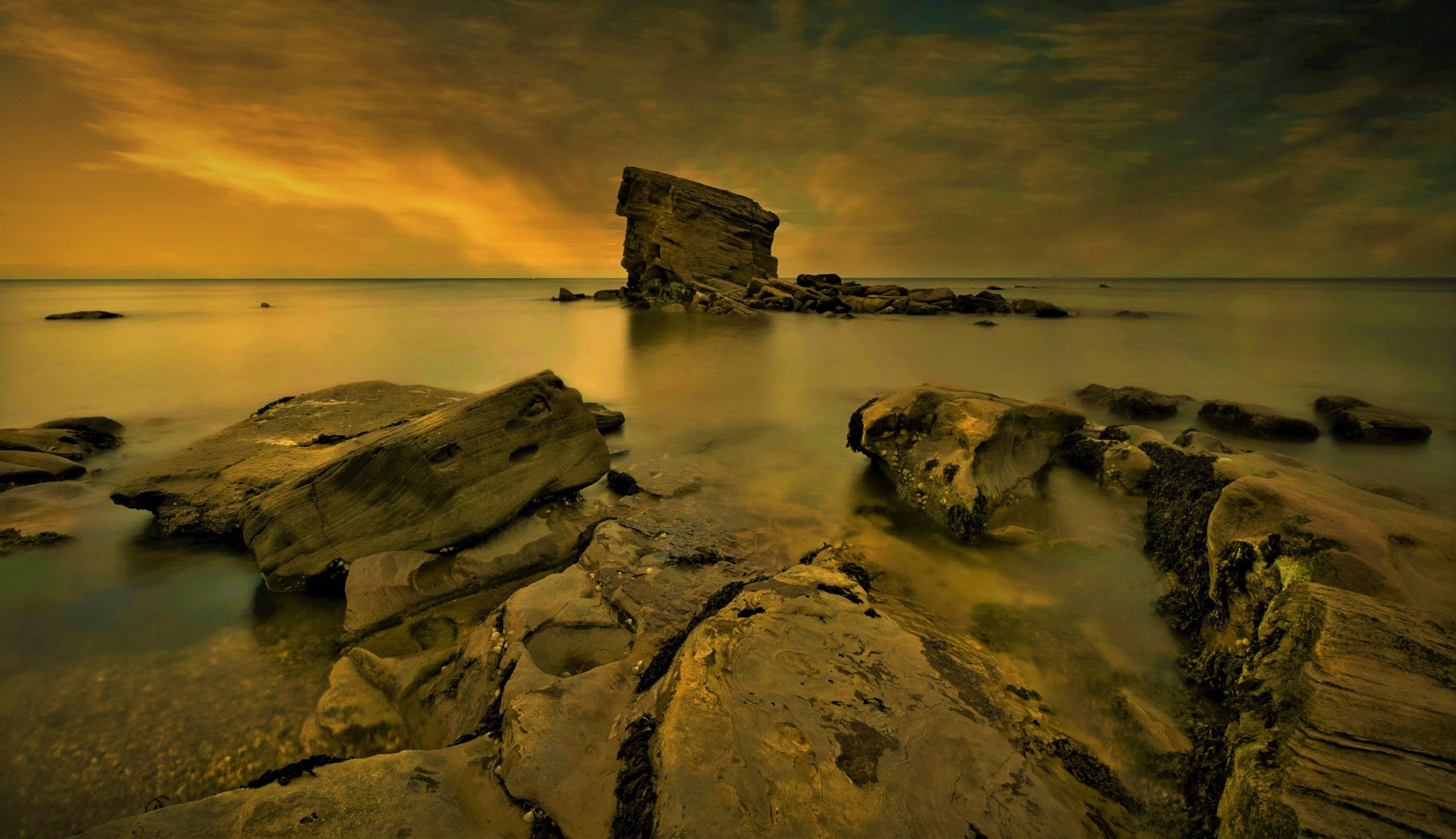 Breathtaking view of rocky coastal landscape during sunset, featuring vibrant skies and tranquil waters.