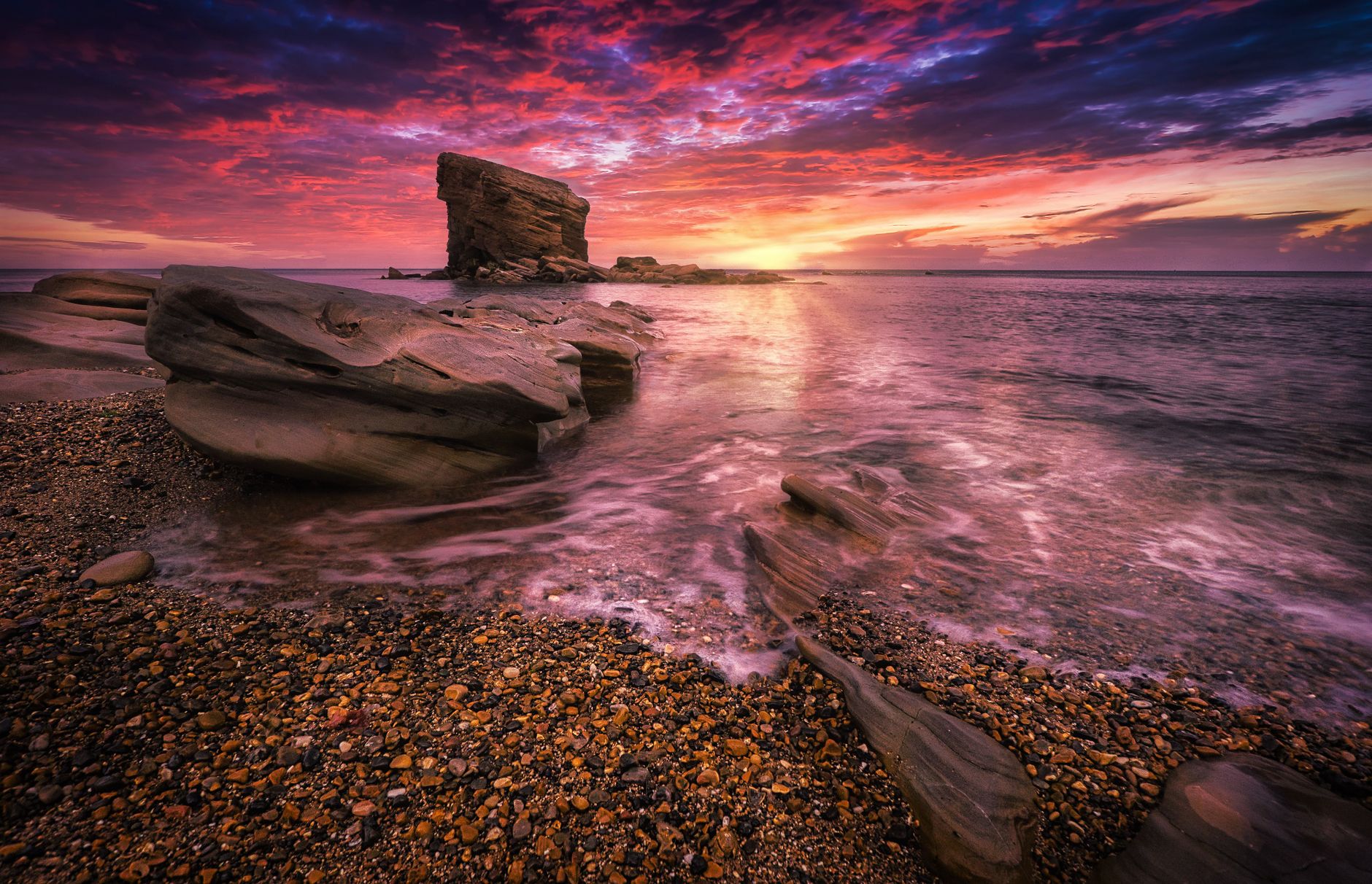 Vivid sunset over a rocky coastline with colorful clouds and eroded formations, creating a dramatic seascape.