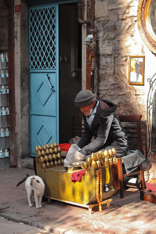 Free Elderly man at outdoor market stall with cat nearby, urban scene. Stock Photo