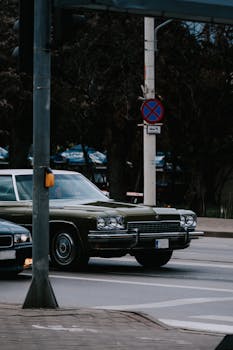 A classic green vintage car waits at a city intersection, embodying retro urban charm.