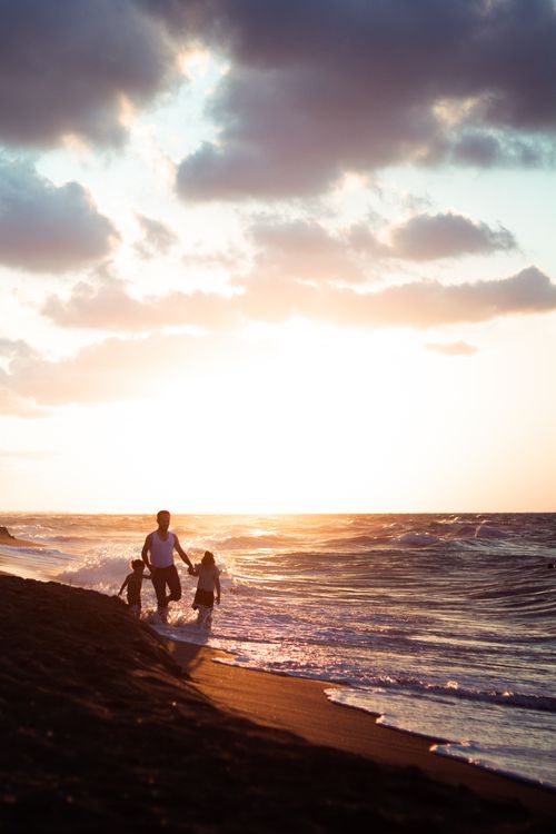 Free Distant father with children holding hands while strolling on sandy coast near waving sea at sundown time on summer evening Stock Photo