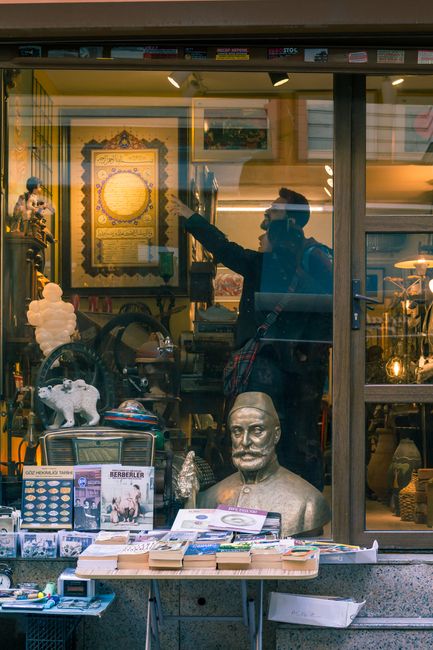 Table with various souvenirs placed near glass showcase of pubic store with assorted goods and sculptures on street in city