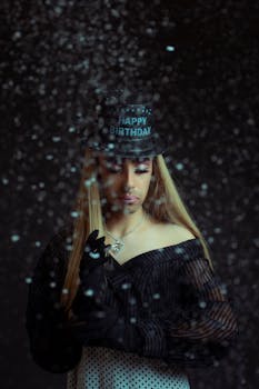 Stylish portrait of a person wearing a 'Happy Birthday' hat surrounded by snowflakes.