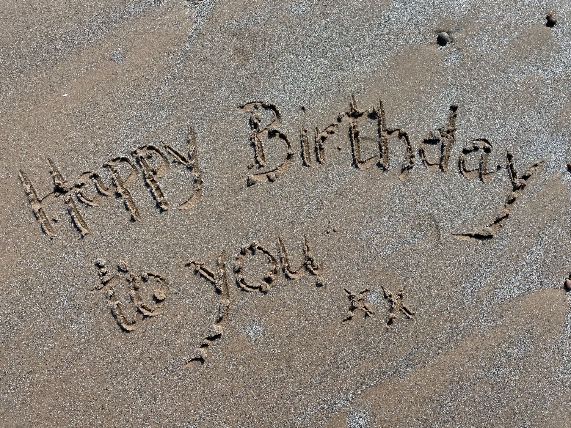 A cheerful birthday message etched in sand on a sunny beach.