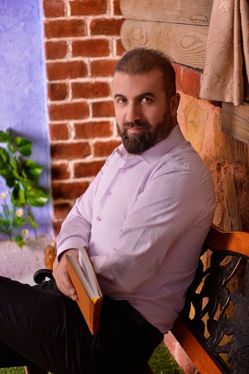 Free A thoughtful bearded man in white attire sitting indoors with a book. Stock Photo