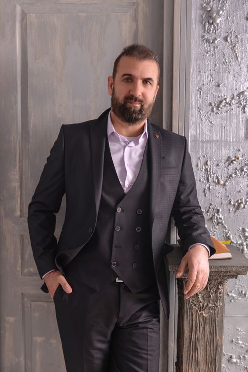 Free Bearded man in a stylish black suit leaning against a textured wall indoors. Stock Photo