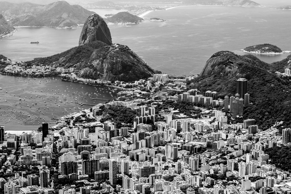 Aerial black and white view of Rio de Janeiro's skyline with Sugarloaf Mountain in the background.