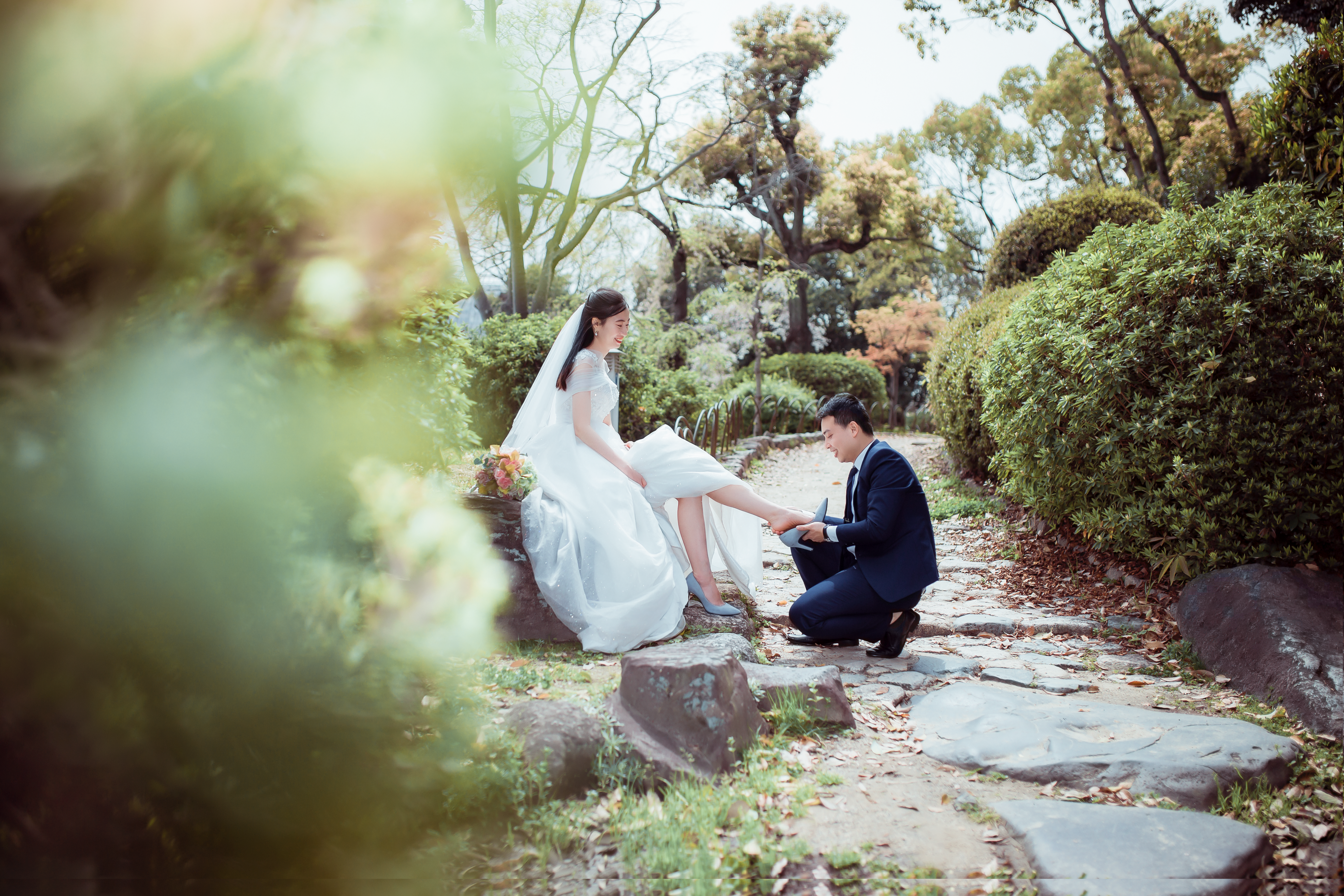 新郎新婦が緑豊かなエリアに囲まれた石の道で優しい瞬間を共有しています。